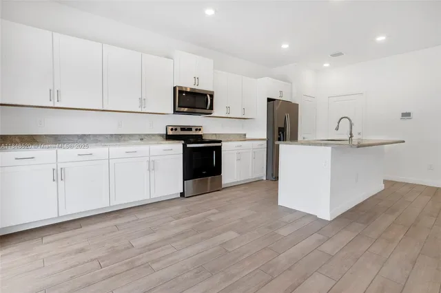 a kitchen with stainless steel appliances granite countertop a stove top oven a sink a refrigerator white cabinets and wooden floor