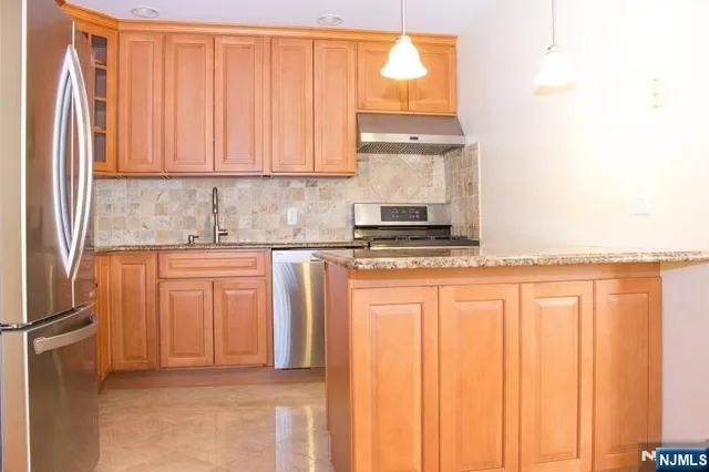 a kitchen with stainless steel appliances granite countertop a refrigerator a sink and white cabinets with wooden floor