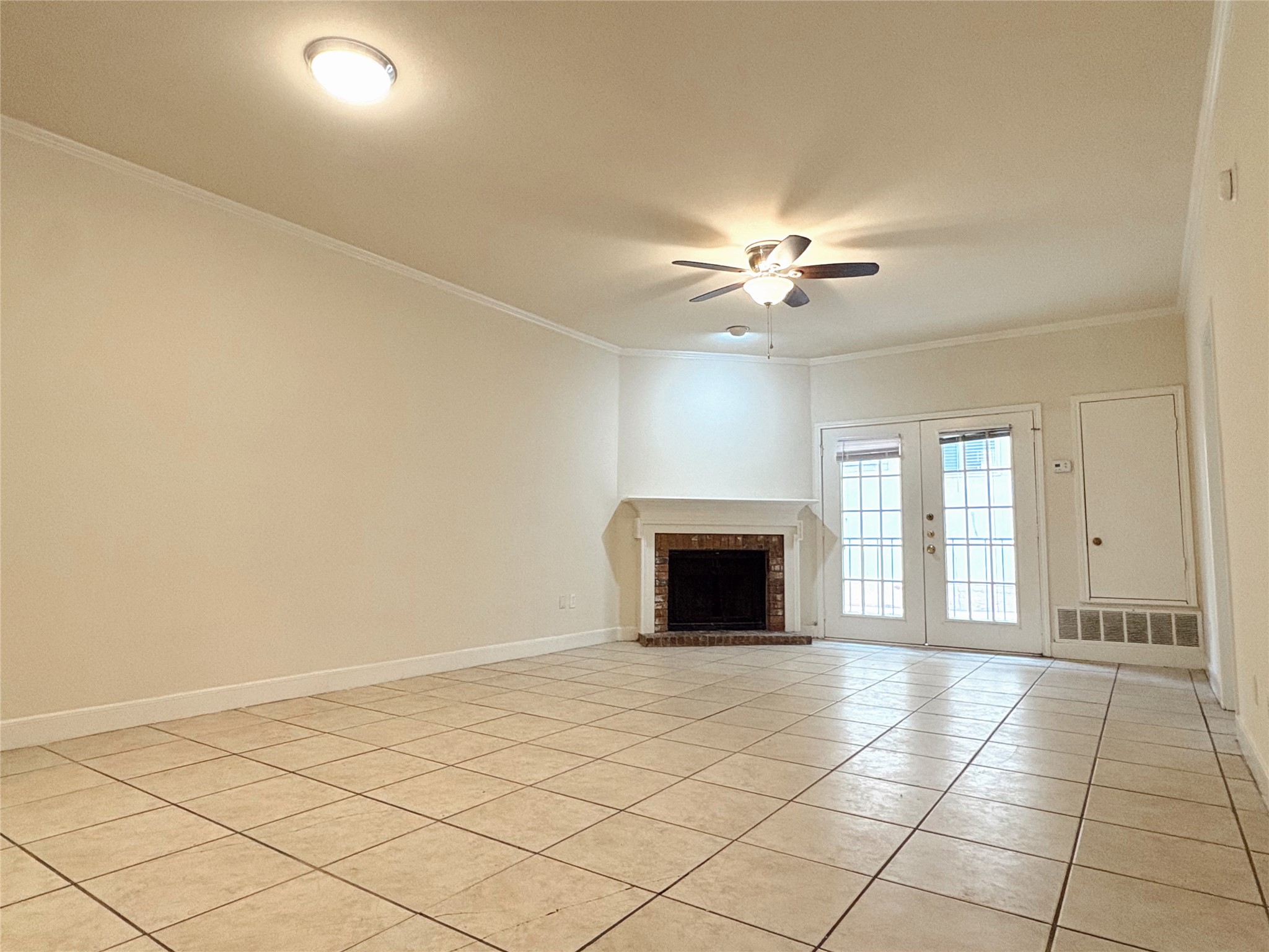 2100 San Gabriel Street, Unit 104 Austin, TX 78705 - Photo 2 of 8 Unfurnished living room with crown molding, light tile patterned floors, a brick fireplace, french doors, and ceiling fan