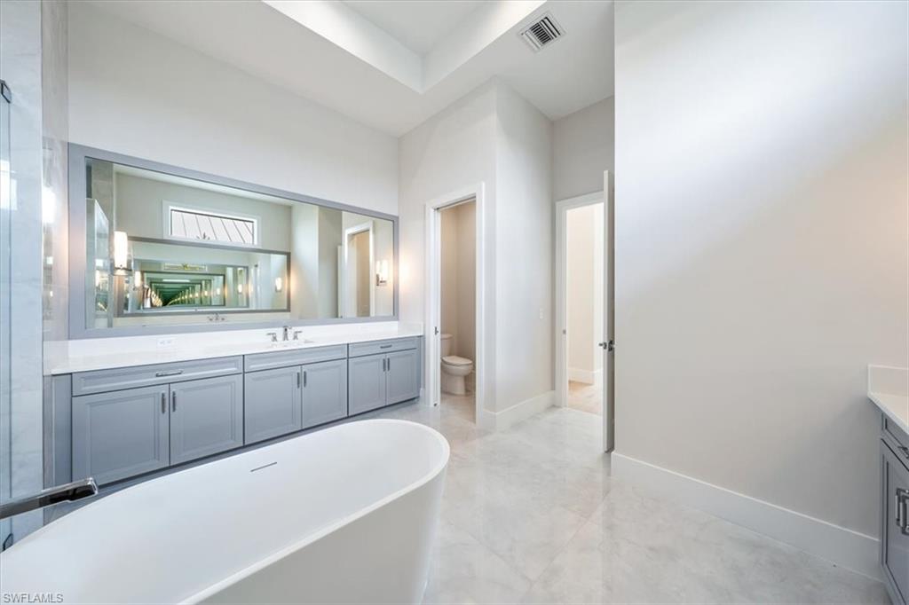 23517 Coconut Road Estero, FL 34134 - Photo 19 of 40 The primary bathroom sparkles with large scale polished tile, oversized dual vanities, soaking tub, and 5-fixture shower with bench and rain showers.