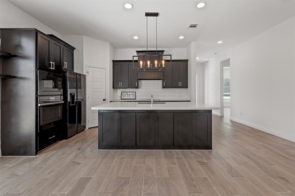 960 Knoxbridge Road Forney, TX 75126 - Photo 4 of 22 Open-concept kitchen featuring an oversized island with an undermount sink, dark cabinetry, stainless steel appliances, and wood-finish flooring