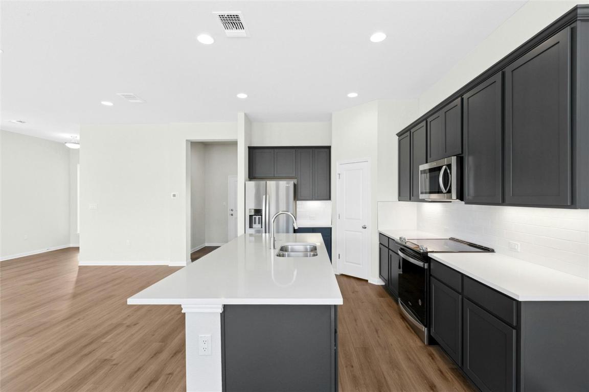320 Creek Road, Unit 302 Dripping Springs, TX 78620 - Photo 3 of 21 Kitchen with stainless steel appliances, decorative backsplash, a center island with sink, light wood finished floors, and recessed lighting