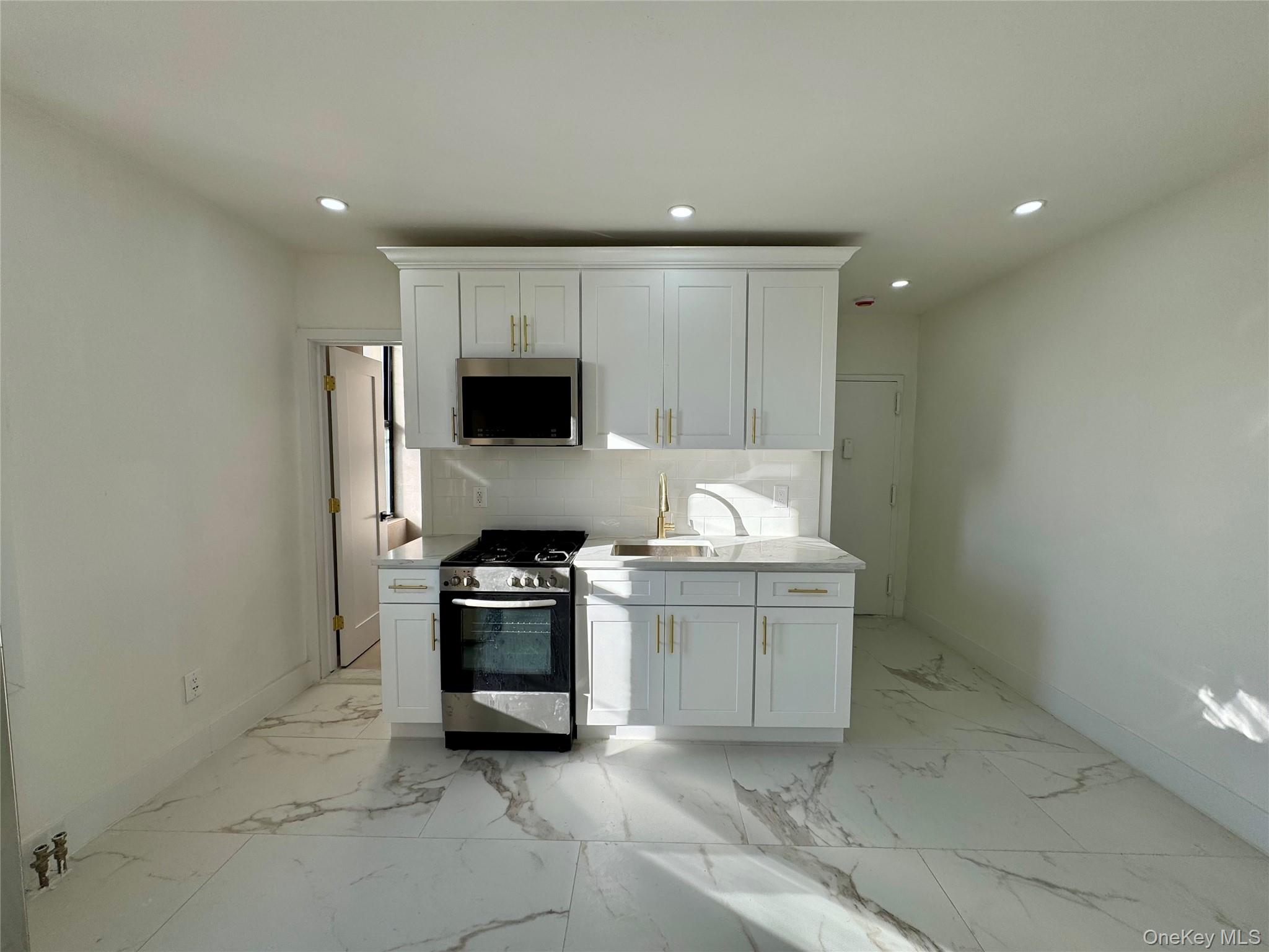 315 Riverside Boulevard, Unit 1 Long Beach, NY 11561 - Photo 1 of 9 Kitchen featuring backsplash, white cabinetry, sink, and appliances with stainless steel finishes