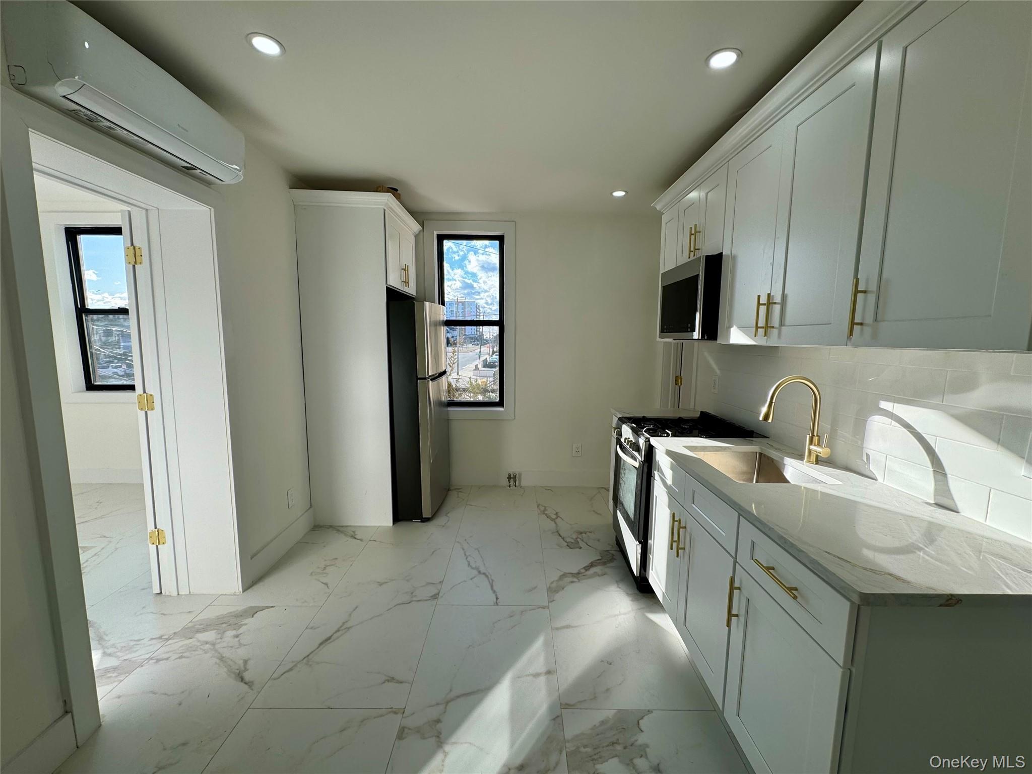 315 Riverside Boulevard, Unit 1 Long Beach, NY 11561 - Photo 2 of 9 Kitchen with sink, stainless steel appliances, light stone counters, a wall unit AC, and backsplash