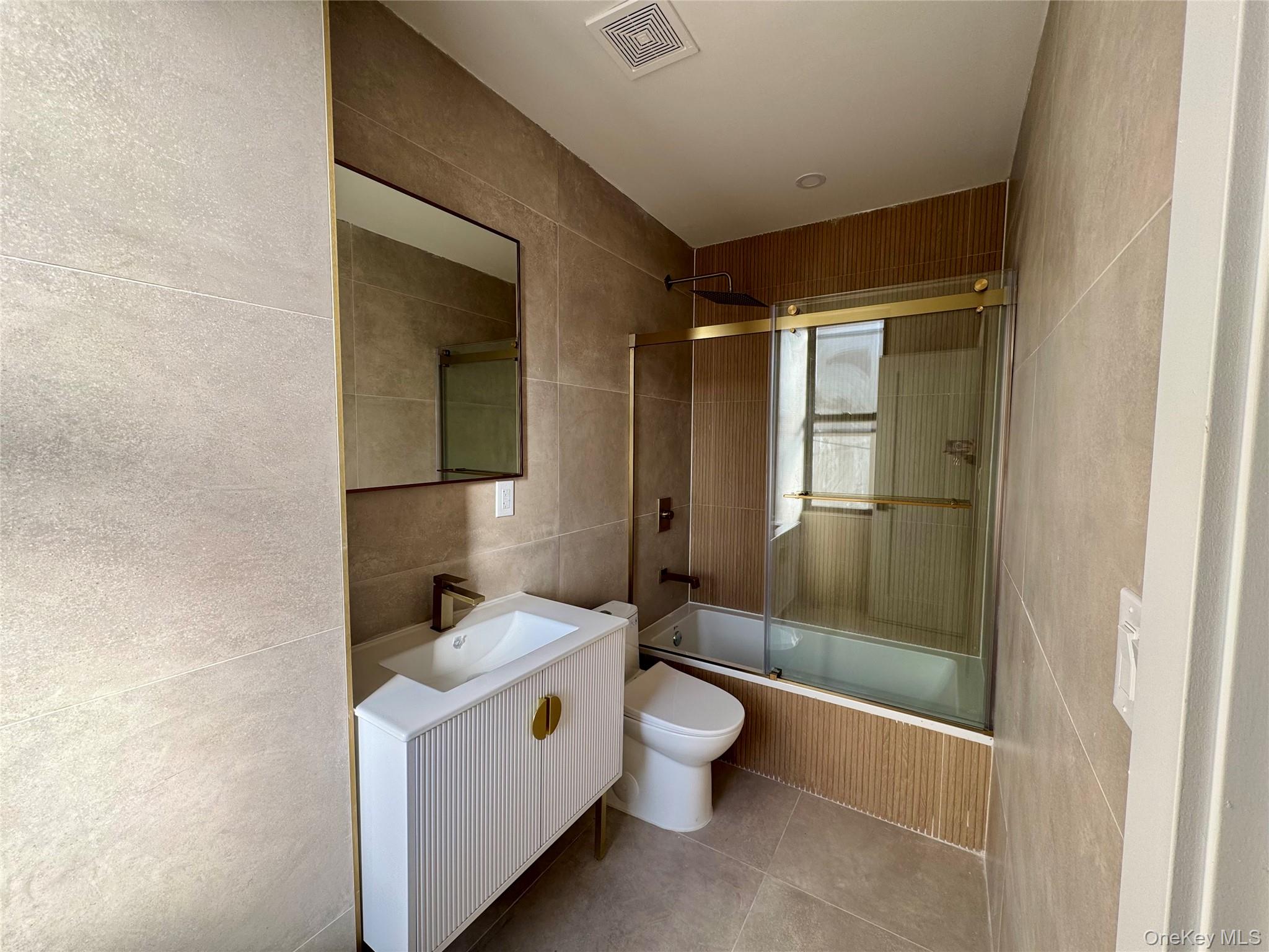 315 Riverside Boulevard, Unit 1 Long Beach, NY 11561 - Photo 4 of 9 Full bathroom with tile patterned floors, bath / shower combo with glass door, toilet, vanity, and tile walls