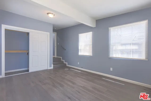 an empty room with wooden floor closet and windows