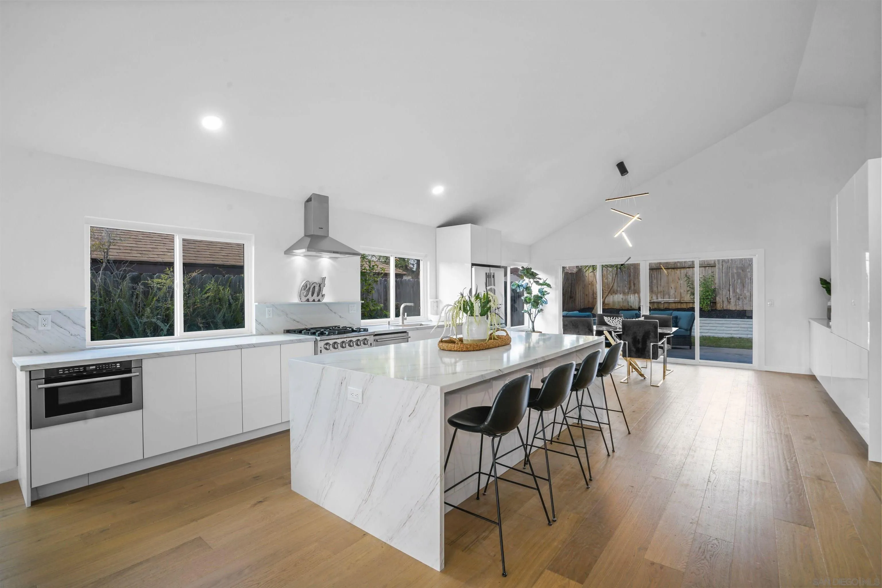 113 Solace Court Encinitas, CA 92024 - Photo 9 of 38 a kitchen with stainless steel appliances kitchen island granite countertop a stove a refrigerator a microwave oven a dining table and chairs with wooden floor