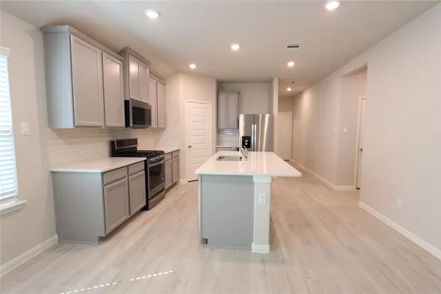 a large kitchen with a large counter top a sink stainless steel appliances and cabinets