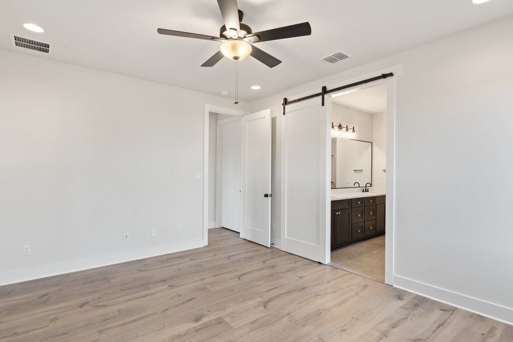711 Paleface Ranch Road, Unit 9 Spicewood, TX 78669 - Photo 9 of 30 Unfurnished bedroom featuring recessed lighting, light wood-style flooring, a barn door, a ceiling fan, and ensuite bath