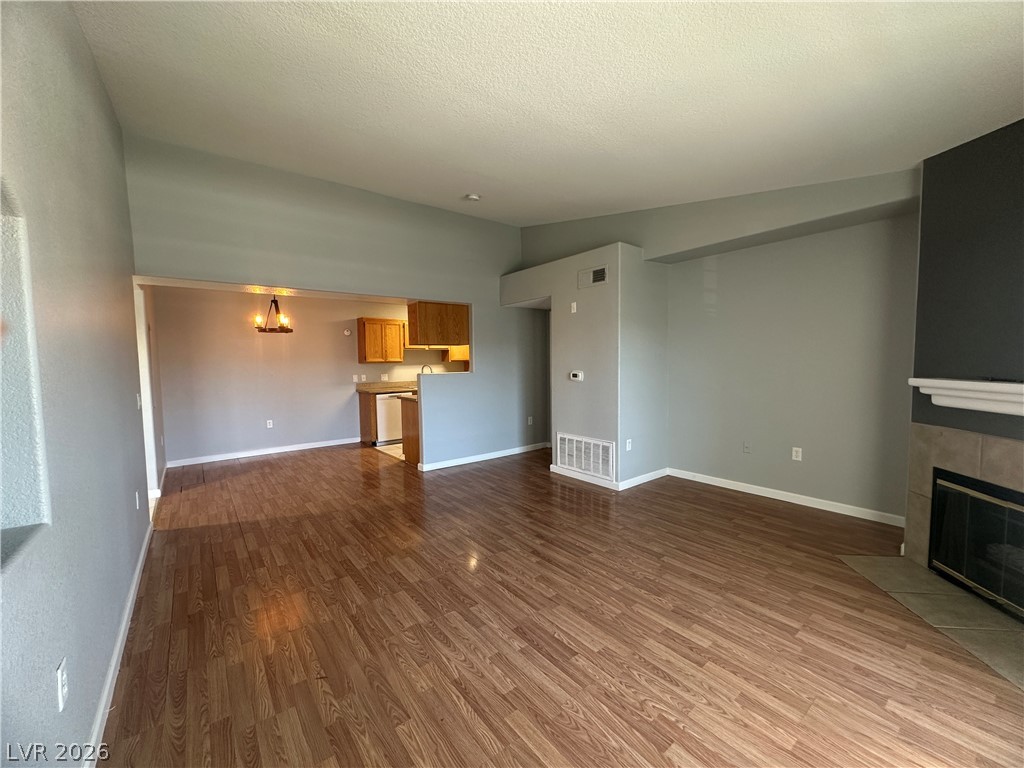 Unfurnished living room featuring dark wood-style floors, a tiled fireplace, and suspended lighting