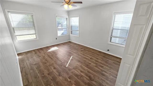 a view of an empty room with wooden floor and window