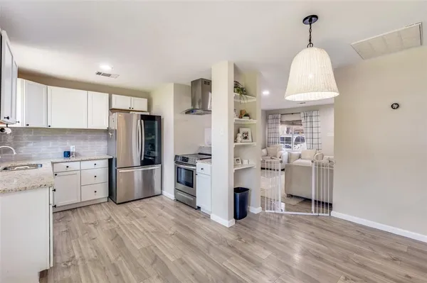 a kitchen with stainless steel appliances a refrigerator a stove a sink dishwasher a oven with white cabinets and wooden floor
