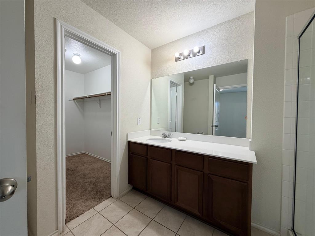 2203 Vance Drive Forney, TX 75126 - Photo 12 of 23 Full bathroom with vanity, a stall shower, a textured wall, a spacious closet, and light tile patterned flooring