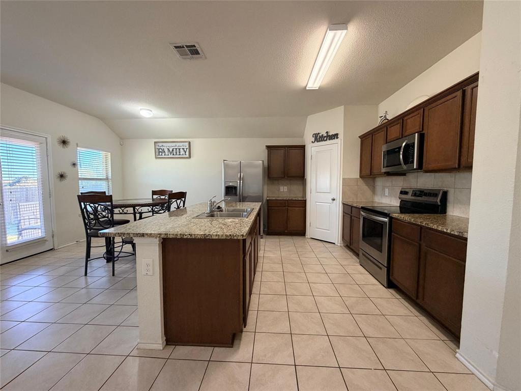 2203 Vance Drive Forney, TX 75126 - Photo 4 of 23 Kitchen with appliances with stainless steel finishes, light tile patterned flooring, decorative backsplash, a center island with sink, and dark brown cabinetry