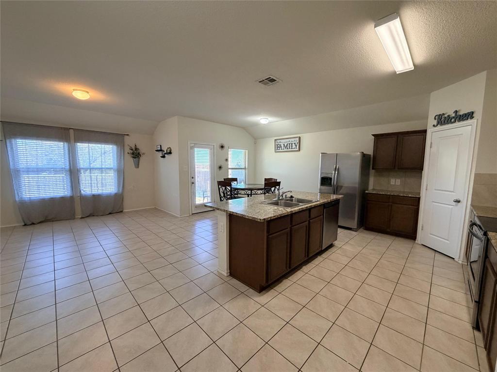 2203 Vance Drive Forney, TX 75126 - Photo 5 of 23 Kitchen featuring dark brown cabinets, stainless steel appliances, plenty of natural light, a center island with sink, and lofted ceiling