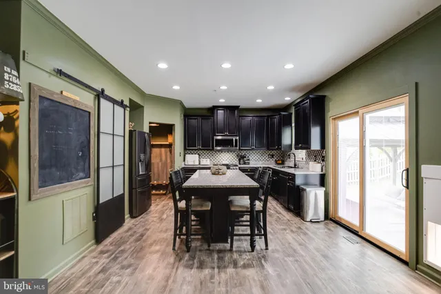 a kitchen with stainless steel appliances granite countertop a refrigerator a sink a stove and a dining table with wooden floor