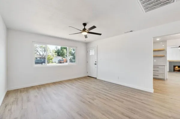 an empty room with wooden floor chandelier fan and windows