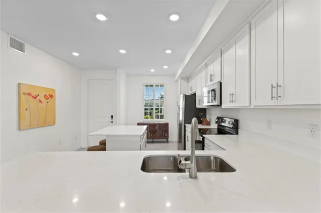 a large white kitchen with kitchen island a stove a sink a refrigerator and white cabinets next to a window