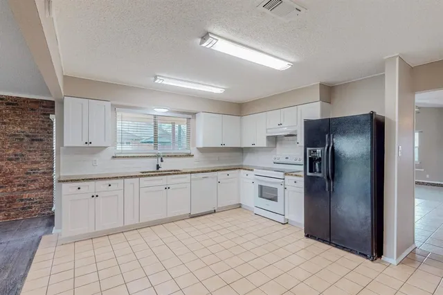 a kitchen with granite countertop white cabinets a refrigerator and a sink