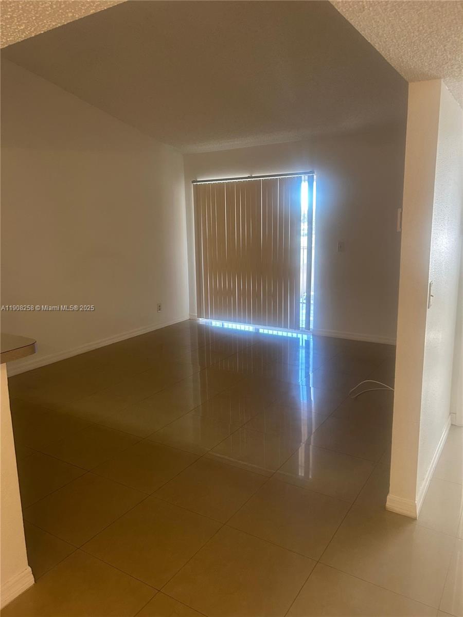 3995 West McNab Road, Unit B310 Pompano Beach, FL 33069 - Photo 2 of 10 an empty room with wooden floor and windows with curtains