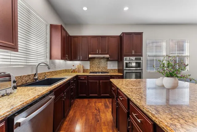 a kitchen with stainless steel appliances granite countertop a sink a stove and a wooden cabinets