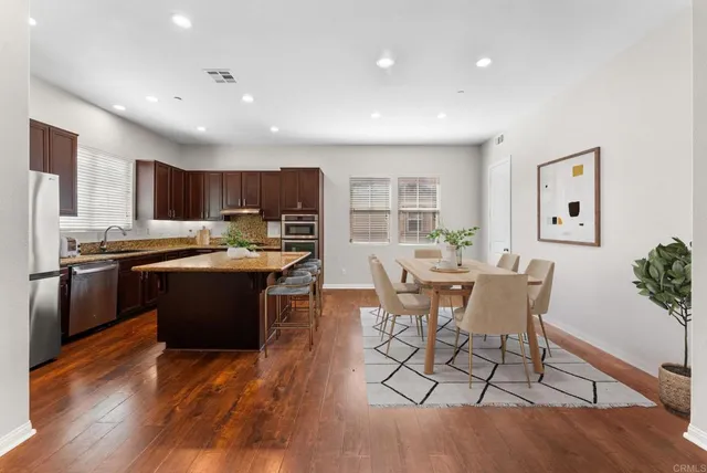 a kitchen with stainless steel appliances kitchen island granite countertop a stove a refrigerator a sink a dining table and chairs with wooden floor