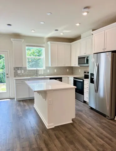 a kitchen with stainless steel appliances a refrigerator a sink dishwasher a stove and white cabinets with wooden floor