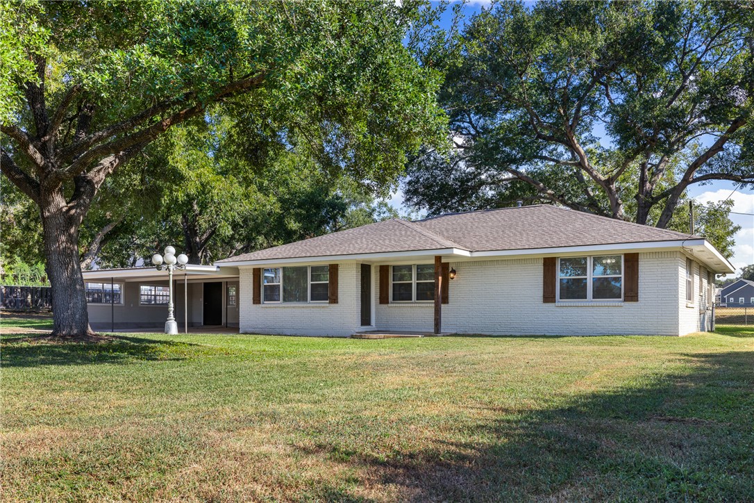 Single story home featuring a front yard, brick siding, a shingled roof, and a patio