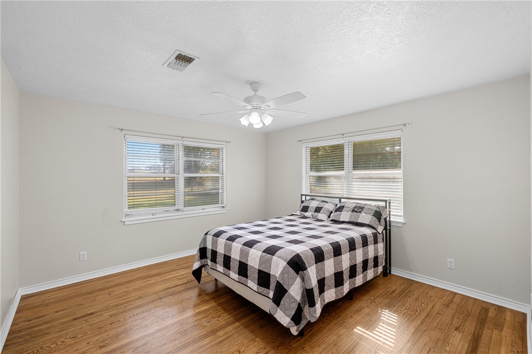 1906 Gun And Rod Road Brenham, TX 77833 - Photo 22 of 30 Bedroom with multiple windows, a textured ceiling, light wood finished floors, and ceiling fan