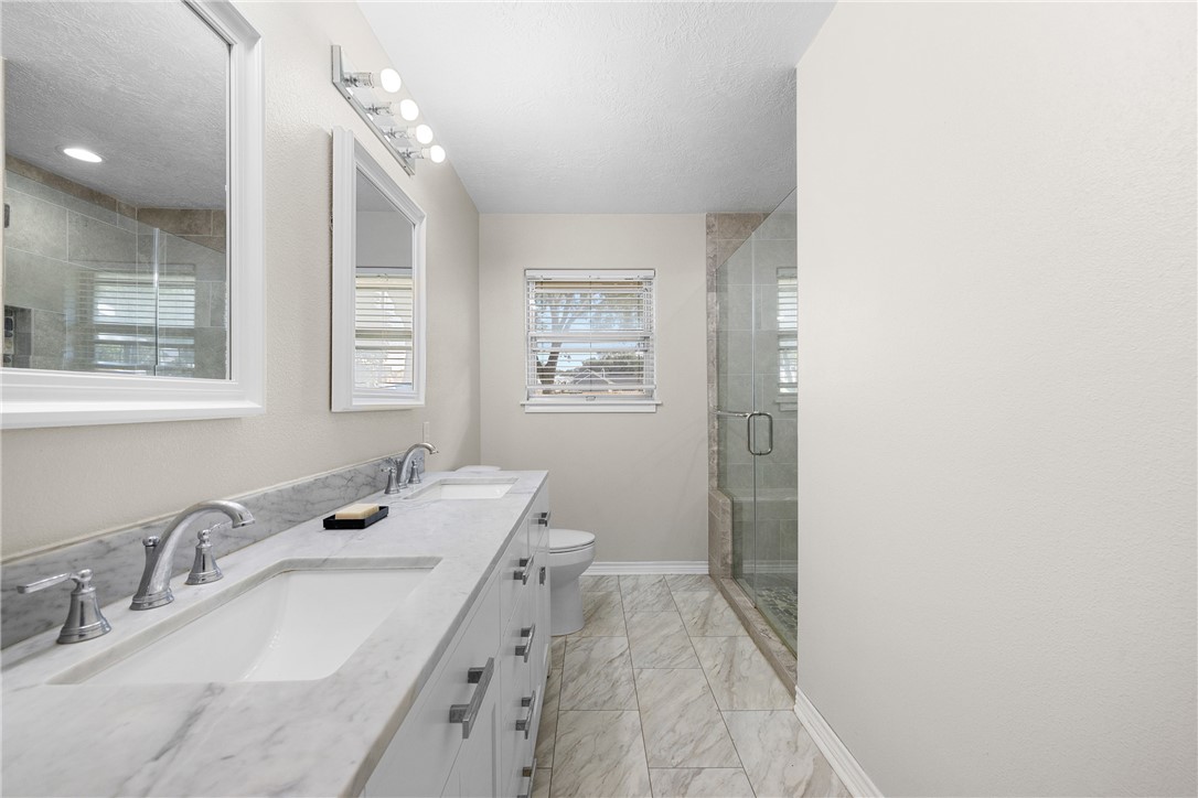 1906 Gun And Rod Road Brenham, TX 77833 - Photo 25 of 30 Full bath with double vanity, a textured ceiling, a stall shower, and light marble finish flooring