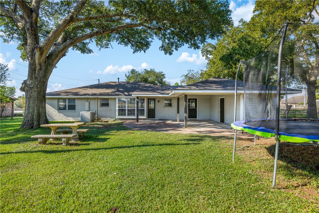 1906 Gun And Rod Road Brenham, TX 77833 - Photo 8 of 30 Rear view of house with a trampoline, a yard, brick siding, a patio area, and an attached carport