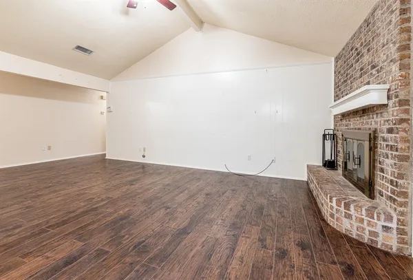 a view of an empty room with wooden floor and a fireplace
