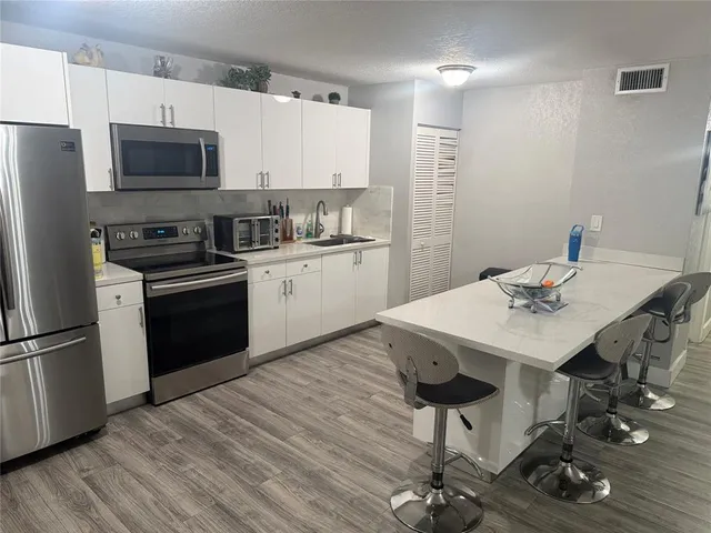 a kitchen with stainless steel appliances a stove a sink dishwasher a refrigerator with a dining table and chairs