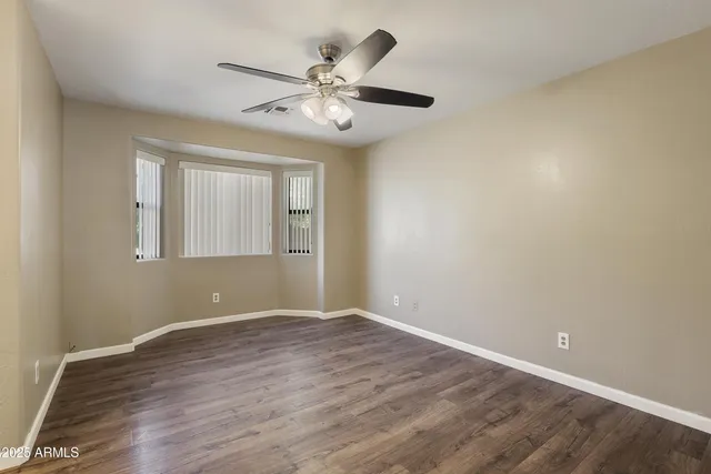 an empty room with wooden floor fan and windows