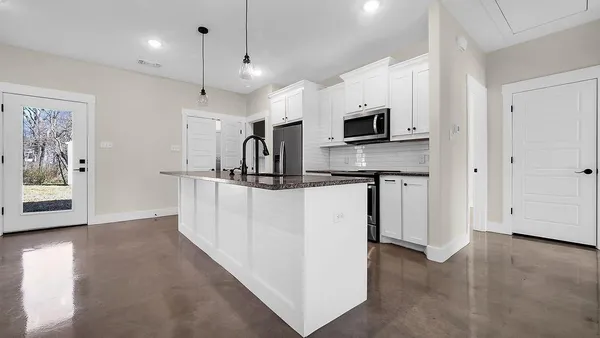 a living room with stainless steel appliances kitchen island a white cabinets and a sink
