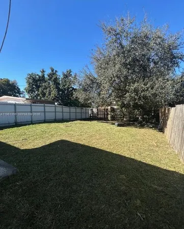 a view of a yard with plants and large trees