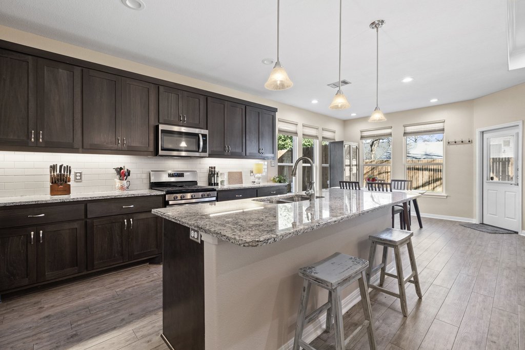 1720 Prather Street Taylor, TX 76574 - Photo 8 of 34 a kitchen with kitchen island granite countertop wooden floors white cabinets and stainless steel appliances