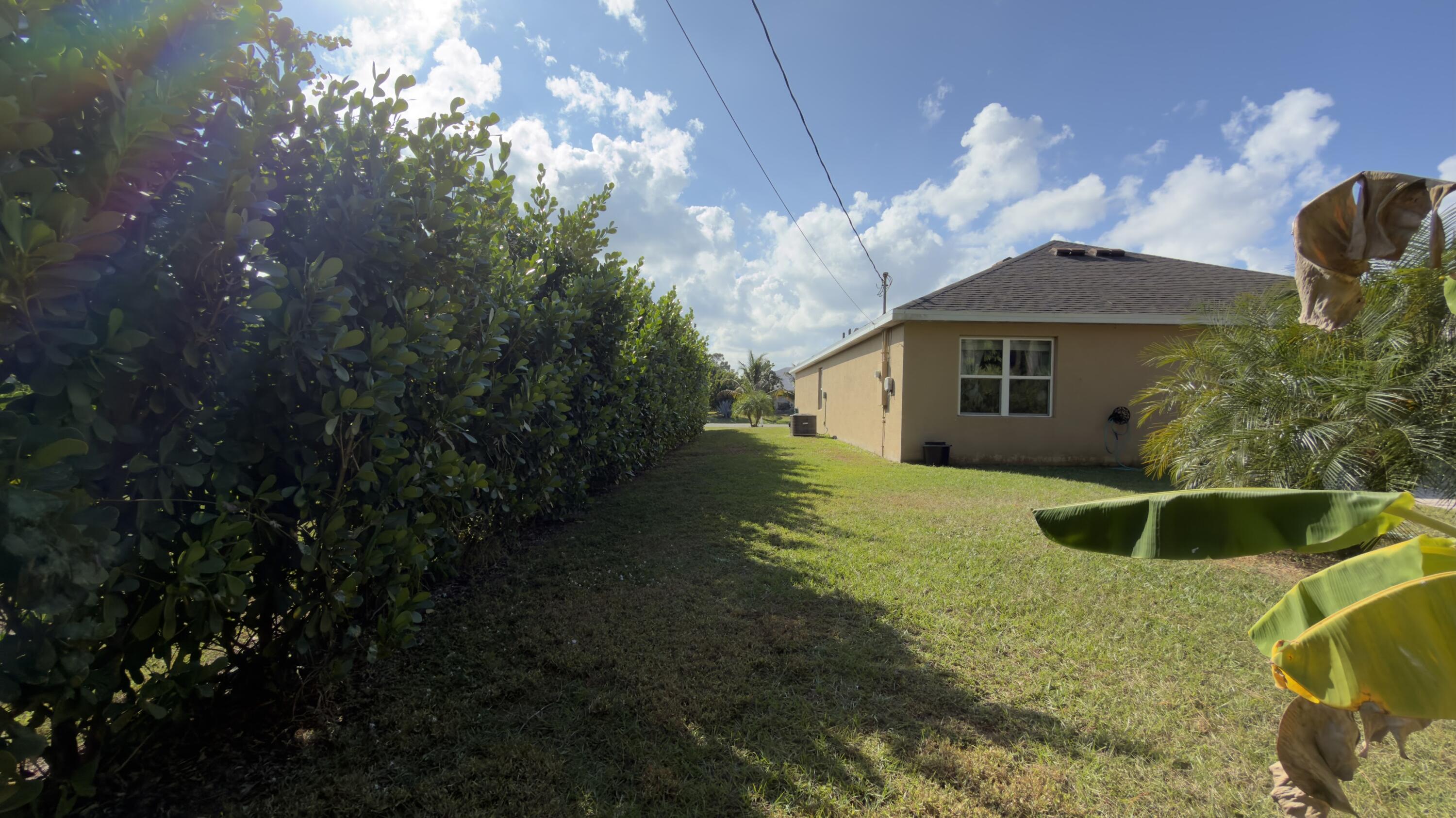 1117 Southwest Goodman Avenue Port St. Lucie, FL 34953 - Photo 15 of 18 a white house with a yard plants and large tree