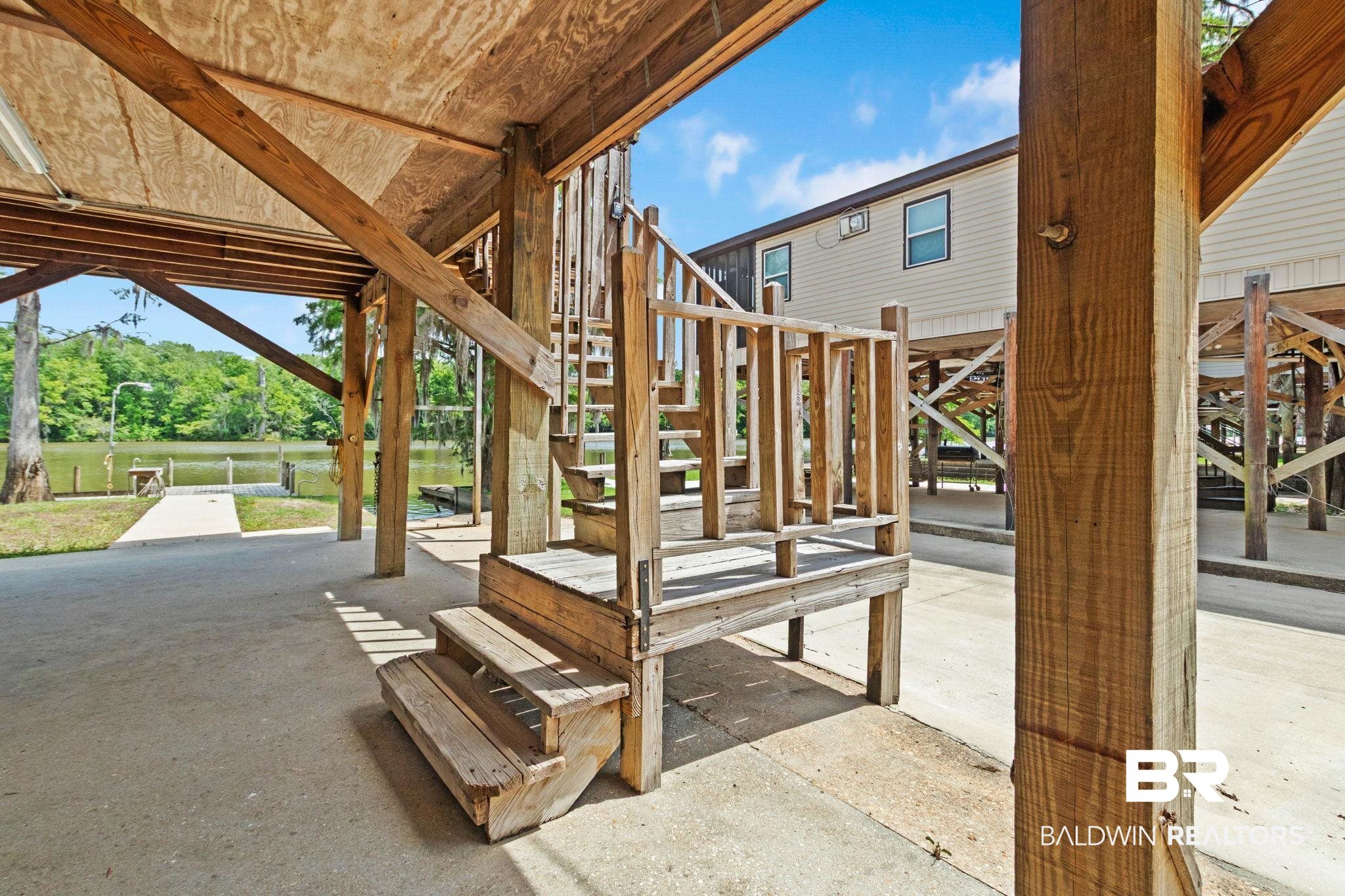 8153 Bryant's Lndg Road Stockton, AL 36579 - Photo 67 of 87 Elevated stilt-style construction featuring an exterior staircase with wood railings, a concrete ground-level pad, and exposed wood support beams