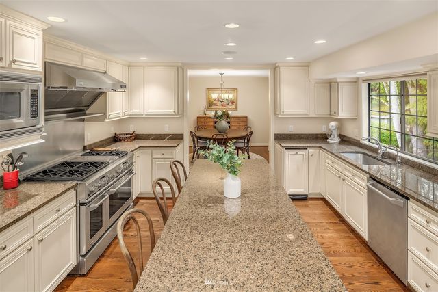 a kitchen with stainless steel appliances granite countertop a stove top oven a sink dishwasher and white cabinets with wooden floor