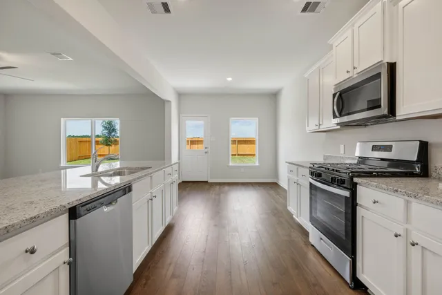 a view of an empty room with wooden floor and a kitchen