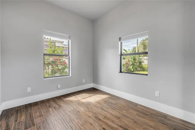 an empty room with wooden floor and windows with curtains