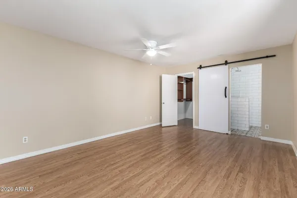 a view of an empty room with wooden floor and a ceiling fan