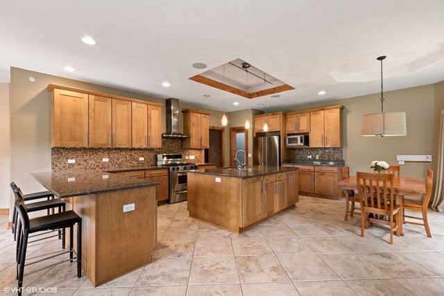 a kitchen with stainless steel appliances kitchen island granite countertop a table chairs and a refrigerator