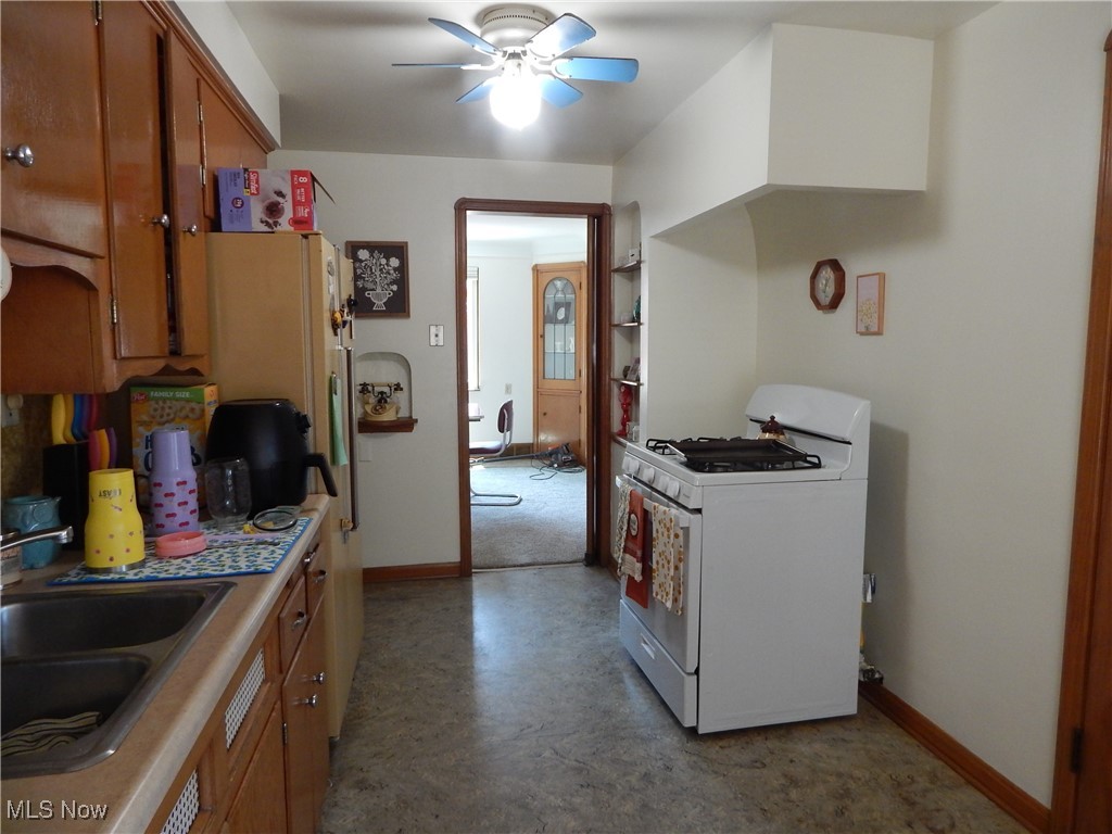 3211 Warren Road Cleveland, OH 44111 - Photo 10 of 32 Kitchen with white range with gas stovetop, a ceiling fan, brown cabinetry, refrigerator, and light countertops
