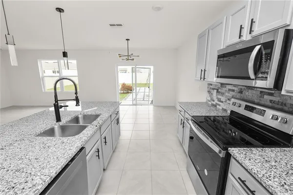 a large kitchen with kitchen island granite countertop a sink a counter top space appliances and cabinets