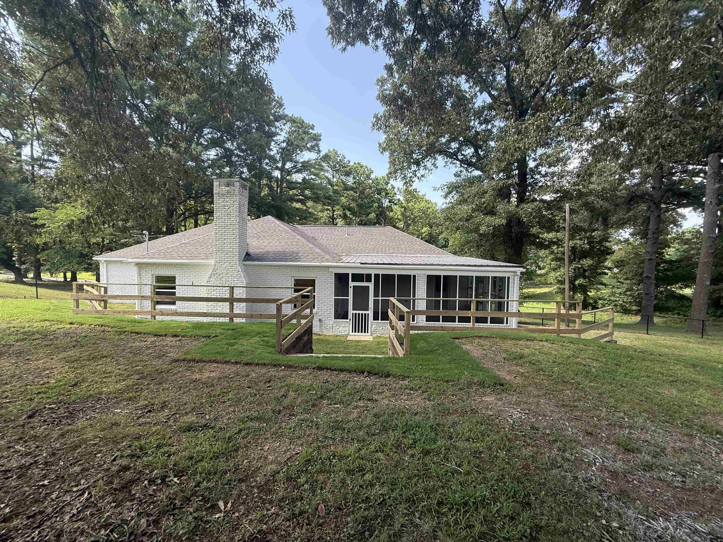 1835 Pleasant Grove Road Moscow, TN 38057 - Photo 29 of 34 White brick ranch-style exterior featuring a covered porch, an attached screened porch, a prominent brick chimney, a wood fence, and mature trees