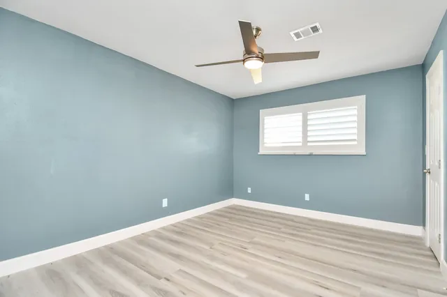 an empty room with wooden floor ceiling fan and windows