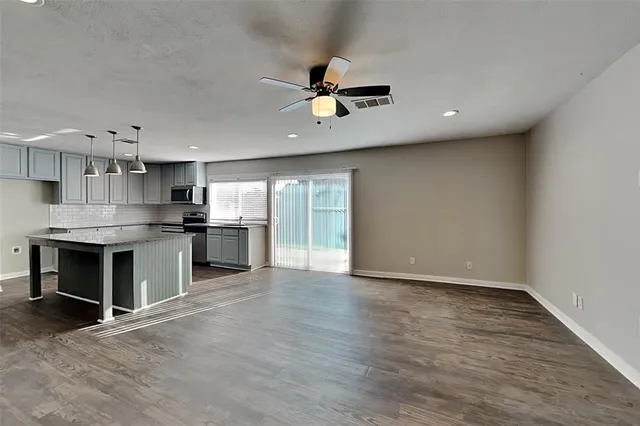 an empty room with wooden floor kitchen and windows
