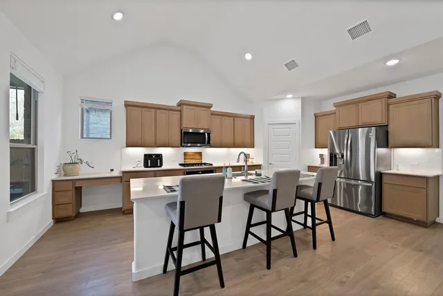 a kitchen with stainless steel appliances kitchen island granite countertop a dining table chairs and a refrigerator